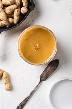 Creamy and smooth peanut butter in jar set, on white stone table background, top view flat lay