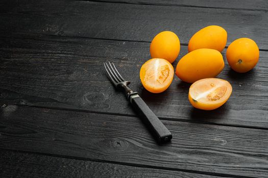Ripe Yellow plum tomatoes set, on black wooden table background, with copy space for text