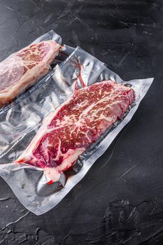 Top blade steak, vacuum packed organic beef for sous vide cooking on black textured background, top view