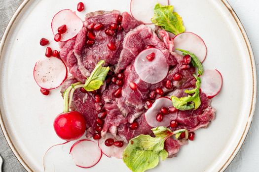 Fresh carpaccio salad with wine vinegar set, with Radish and garnet, on plate, on white stone background, top view flat lay