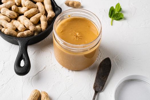 Jar with peanut butter with peanuts set, on white stone table background