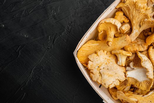 Cantharellus cibarius, commonly known as the chanterelle set, in wooden box container, on black dark stone table background, top view flat lay, with copy space for text