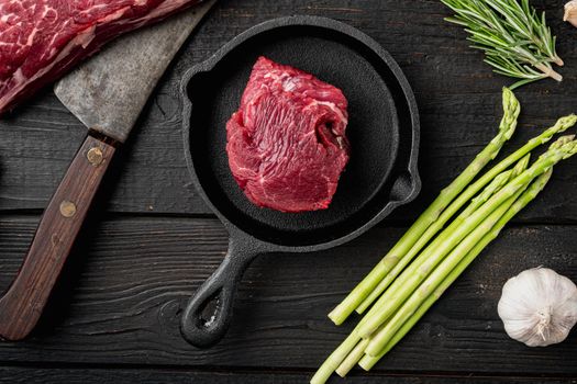 Raw beef fillet steaks with spices set, on frying cast iron pan, on black wooden table background, top view flat lay