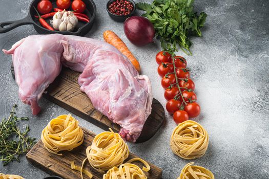 Raw rabbit meat with fresh vegetables ready for cooking set, on gray stone background, with copy space for text