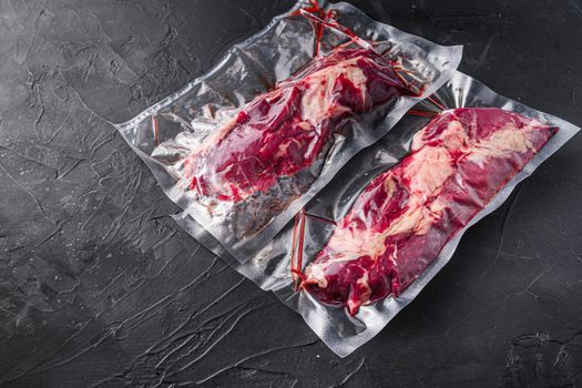 Chuck Tenders beef steak in vacuum sealed bag on black textured background side view space for text