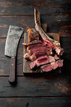 Sliced medium rare grilled Beef steak set, tomahawk cut, on wooden serving board, on old dark wooden table background, with copy space for text