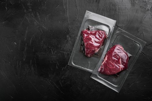 Beef steak vacuum sealed set, on black dark stone table background, top view flat lay, with copy space for text
