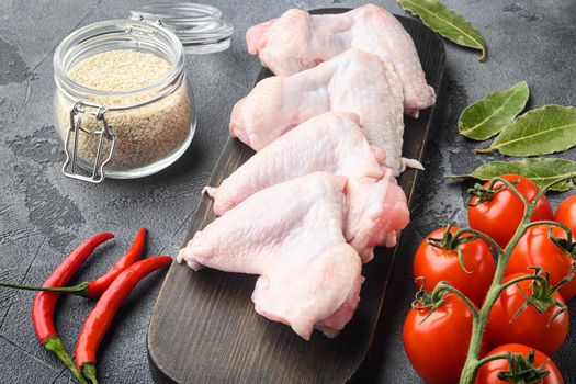 Fresh raw chicken wings with spices and herbs set, and sesame, on wooden cutting board, on gray background