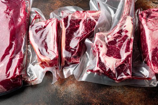 Vacuum packed organic raw beef classic cuts set, tomahawk, t bone, club steak, rib eye and tenderloin cuts, on old dark rustic background