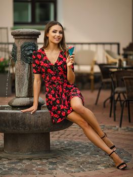 attractive caucasian female in short dress and high heel shoes sitting on the small fountain