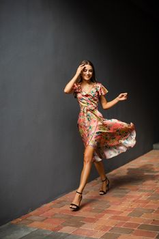 cheerful caucasian female with long dark hair wearing dress walking outside