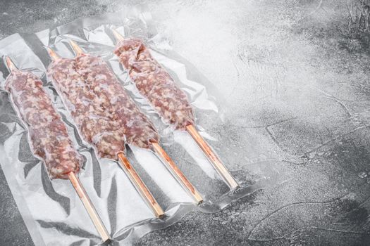 Vacuum packed raw meat skewers set, on gray stone table background, with copy space for text