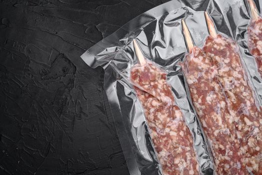 Vacuum packed raw meat skewers set, on black dark stone table background, top view flat lay, with copy space for text