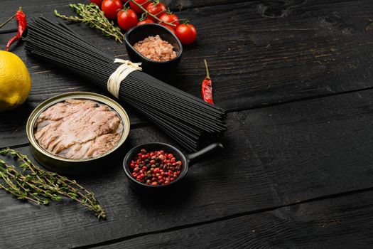 Ingredients uncooked pasta with tuna and tomatoes set, on black wooden table background, with copy space for text