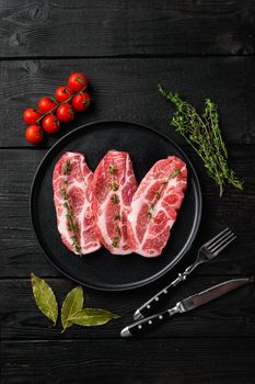 Raw pork neck chop meat with herb leaves and spice set, on black wooden table background, top view flat lay