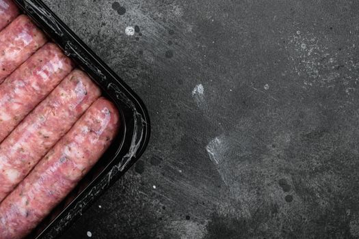 Uncooked meat sausages in plastic pack set, on black dark stone table background, top view flat lay, with copy space for text