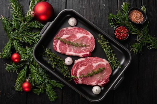 Raw rib eye beef steak with pepper and herbs to the Christmas and New Year set, on black wooden table background, top view flat lay