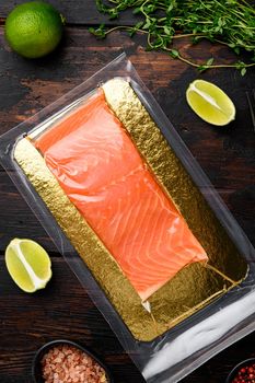 Vacuum packed salmon portion fillet set, with herbs, on old dark wooden table background, top view flat lay