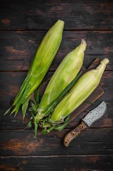 Ripe corn set, on old dark wooden table background, top view flat lay