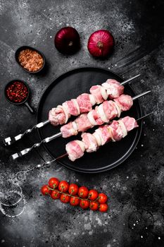 Raw pork shish kebab. BBQ meat with vegetables set, top view flat lay, with copy space for text, on black dark stone table background