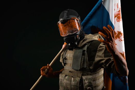 a male soldier in military uniform in a bloody gas mask holds a bloodstained flag of Russia on a black background