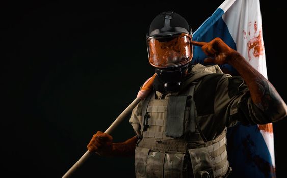 a male soldier in military uniform in a bloody gas mask holds a bloodstained flag of Russia on a black background