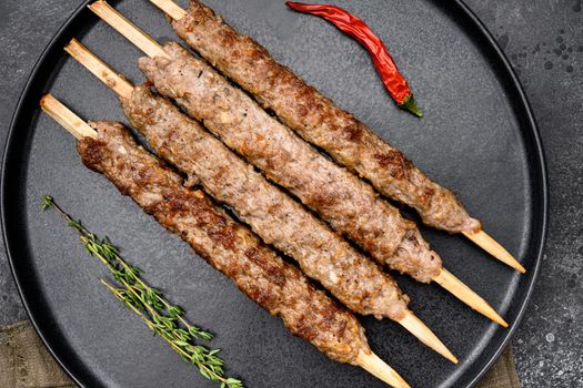 Mutton kebab shish skewers set, on plate, on black dark stone table background, top view flat lay