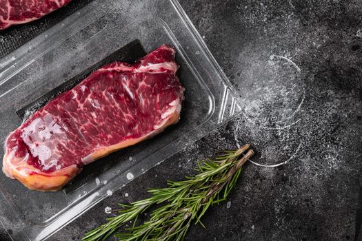 Raw marbled beef steaks in vacuum pack set, on black dark stone table background, top view flat lay, with copy space for text