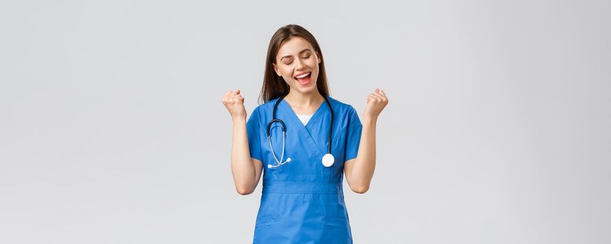 Medical workers, healthcare, covid-19 and vaccination concept. Happy cheerful female nurse, pretty enthusiastic doctor in blue scrubs, passed test, fist pump in rejoice, smiling relieved.