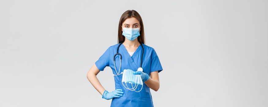 Covid-19, preventing virus, health, healthcare workers and quarantine concept. Young doctor or female nurse in blue scrubs and protective equipment against coronavirus infection, give medical masks.
