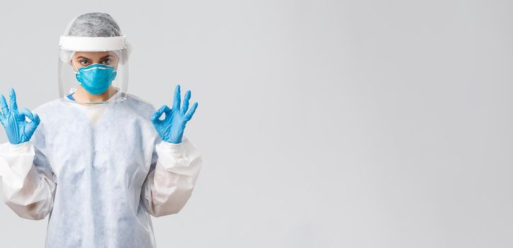 Covid-19, preventing virus, health, healthcare workers and quarantine concept. Confident doctor or nurse in protective equipment PPE, respirator, medical gloves show okay gesture.