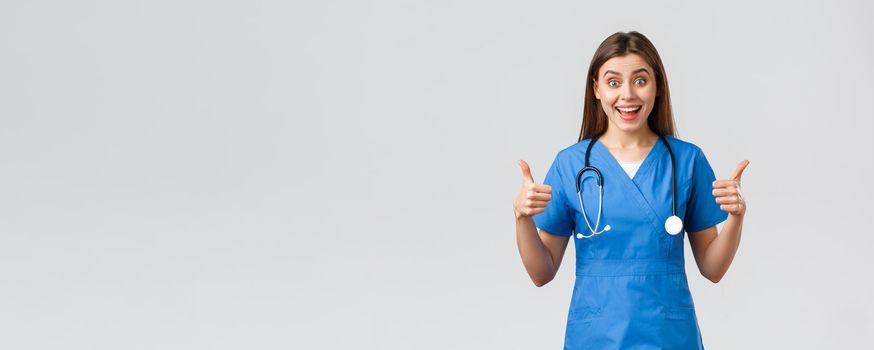 Medical workers, healthcare, covid-19 and vaccination concept. Enthusiastic and upbeat female nurse, doctor in blue scrubs, think wonderful idea, show thumbs-up in approval.