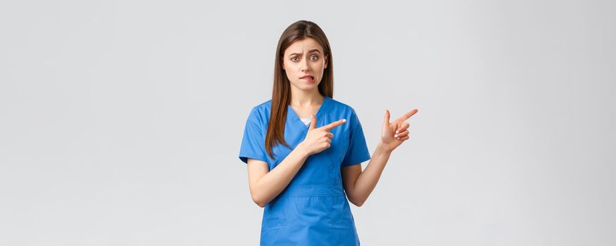 Healthcare workers, prevent virus, insurance and medicine concept. Nervous female intern worried standing in hospital. Doctor or nurse nervously biting lip and pointing fingers right.