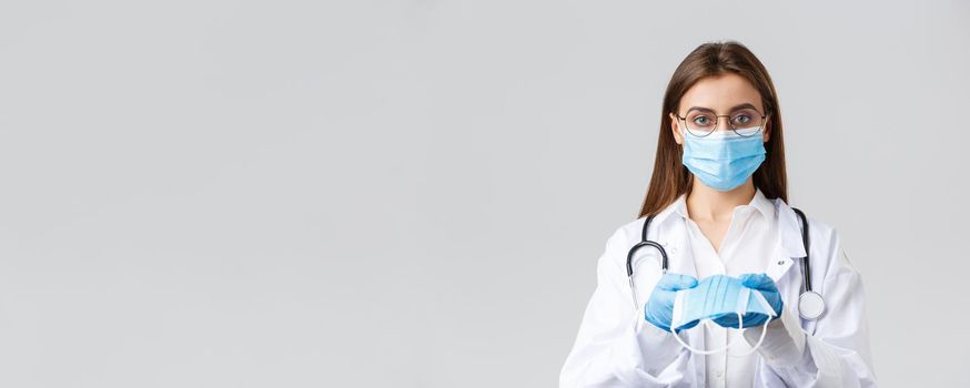 Covid-19, preventing virus, clinic, healthcare workers and quarantine concept. Young doctor in medical mask and gloves, white scrubs, giving face mask protection to patients, look serious.