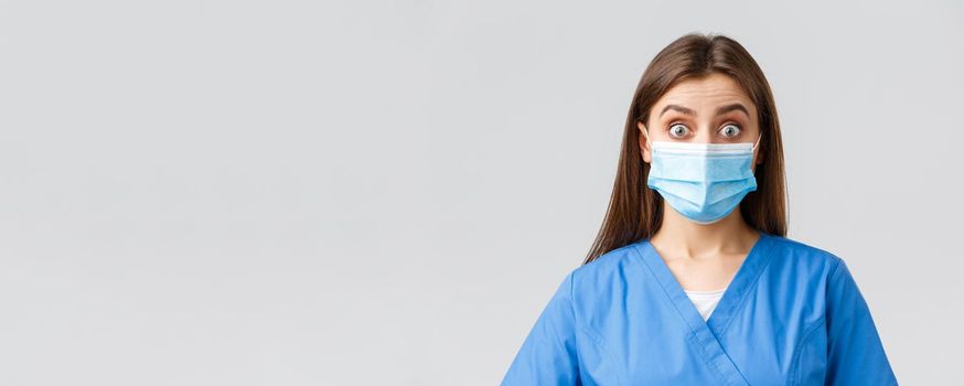 Covid-19, preventing virus, health, healthcare workers and quarantine concept. Surprised female nurse or doctor in blue scrubs and medical mask, staring shocked and excited at camera.
