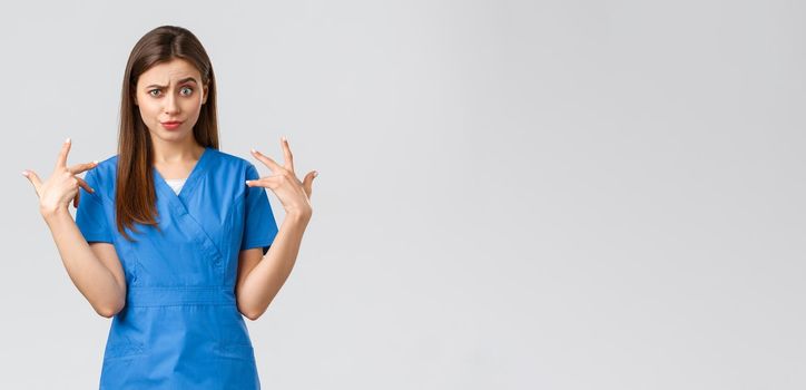 Healthcare workers, prevent virus, insurance and medicine concept. Funny displeased female nurse in blue scrubs grimacing, freak out over something, mimicking and staring camera shocked.