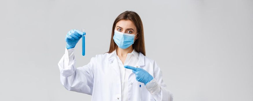 Covid-19, preventing virus, healthcare workers and quarantine concept. Doctor in personal protective equipment, medical mask and scrubs, pointing finger at test-tube coronavirus vaccine.