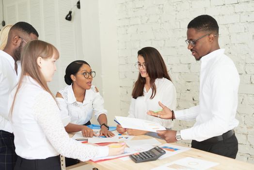 A team of multiethnic people are discussing business in the office. The employees of the company communicate, looking at the schedules and discussing the further strategy.