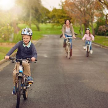 Shot of a mother and her two young children riding their bicycles outside.