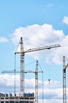 Construction site background with copy space. Industrial building cranes on background of cloudy sky. Hoisting cranes for creating multi-storey buildings of new city districts.