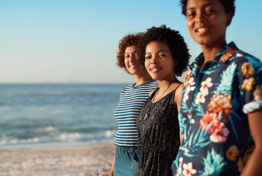 Portrait of an attractive young trio of women standing together and posing on the beach during the day.