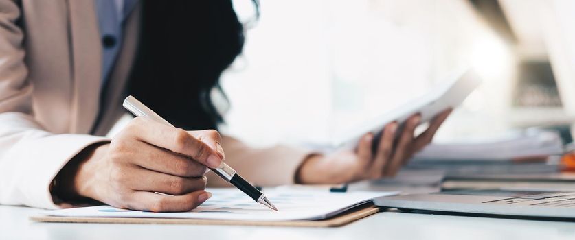 businesswoman or accountant pen pointing on graph chart while using calculator to calculate income tax and corporate income in office.