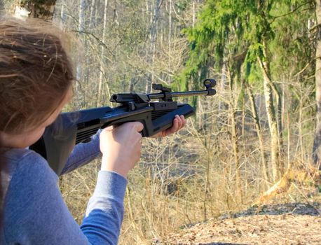 The girl shoots from an air rifle at a target in the forest.