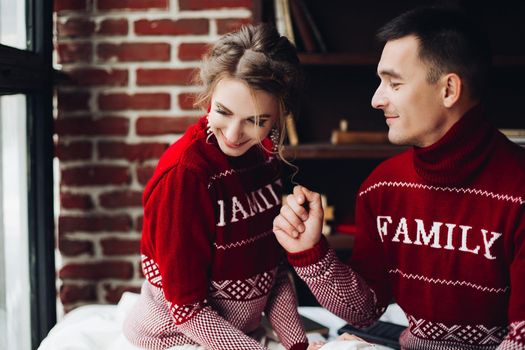 Sensuality couple in red sweaters having fun together, smiling, posing at studio. Boyfriend touching hair of his pretty girlfriend. Happy family celebrating new year and x mas together.