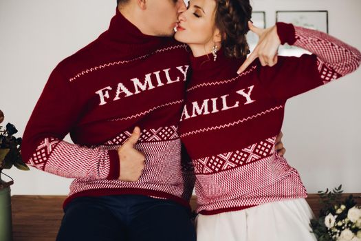 Young funny couple in red sweaters having fun together, smiling, pointing by fingers and making face. Boyfriend with girlfriend celebrating new year together. Christmas look.