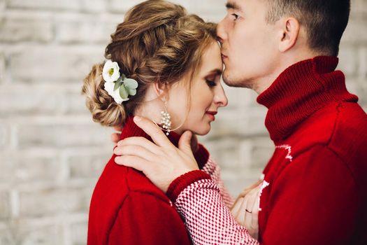Sensuality couple in red sweaters having fun together, smiling, posing at studio. Boyfriend touching hair of his pretty girlfriend. Happy family celebrating new year and x mas together.