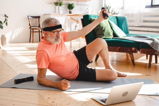 Senior man doing fitness exercises with virtual class and holding dumbbells - wellbeing and wellness