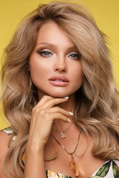 Portrait of sexy young blonde with makeup and hairstyle looking at camera and posing in studio. Beautiful woman wearing accessories standing on yellow isolated background. Concept of beauty.