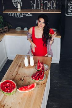 Adorable pregnant woman standing at kitchen and touching big belly with hands. Attractive brunette expecting little child and enjoying motherhood. Concept of love and pregnancy.