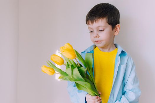 A boy with a bouquet of tulips lifestyle . Postcard for March 8. Congratulations on Women's Day. Congratulations on Mother's Day. Flowers are tulips. Baby and flowers